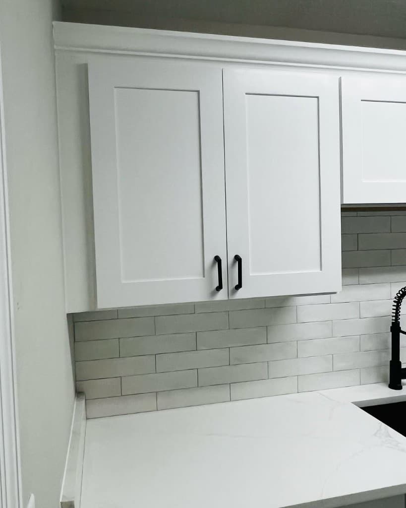 Kitchen detail with white shaker cabinets, subway tile backsplash, and light countertop with black faucet—example of our workmanship.
