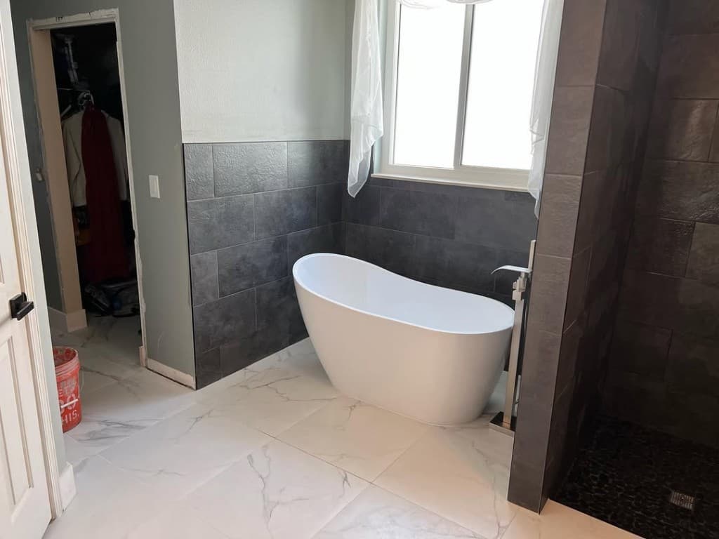 Bathroom oval freestanding tub charcoal wall tile halfway sage paint window shear curtains marble porcelain floor doorway bucket.