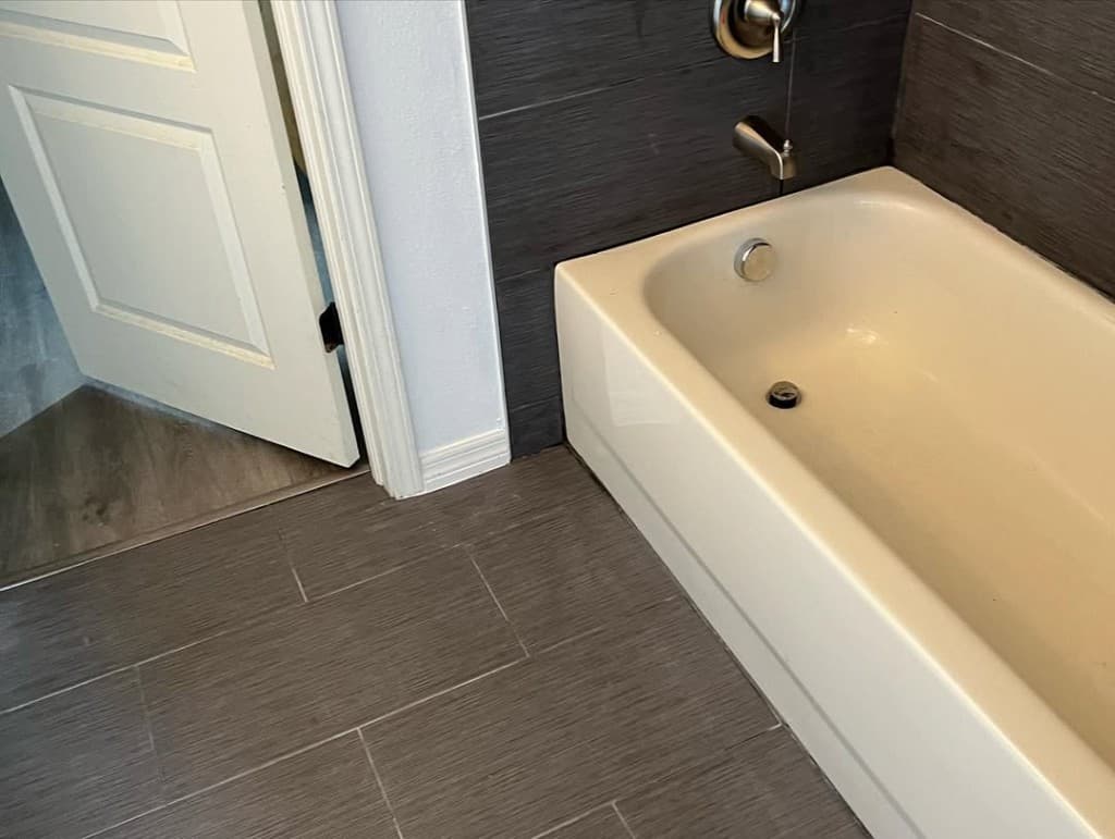Bathtub alcove dark grey wall tiles matching floor satin nickel filler valve white door casing wood floor transition doorway.