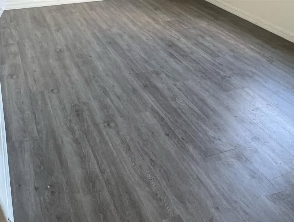 Grey plank floor diagonal stagger white baseboards left top corner bright walls modern LVP documentary photo.
