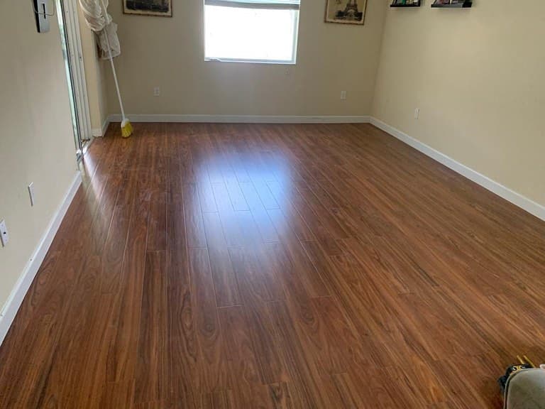 Living space dark brown plank flooring empty sliders left window center beige walls framed art outlets bright.