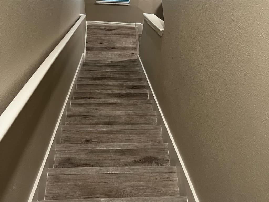 Downward-facing stairs greige plank flooring white skirts handrail taupe drywall clean transition second floor doorway.