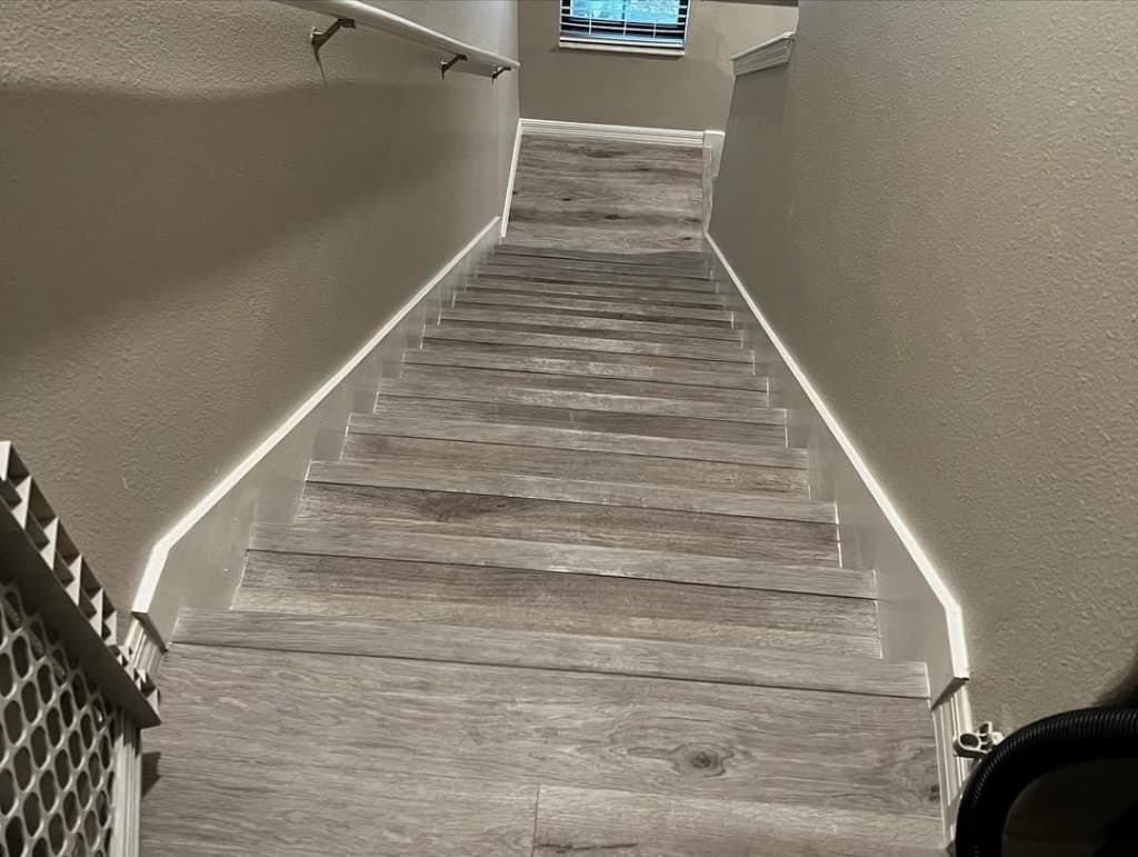 Top-down staircase grey vinyl plank treads landing white baseboards walls neutral greige airy window natural.