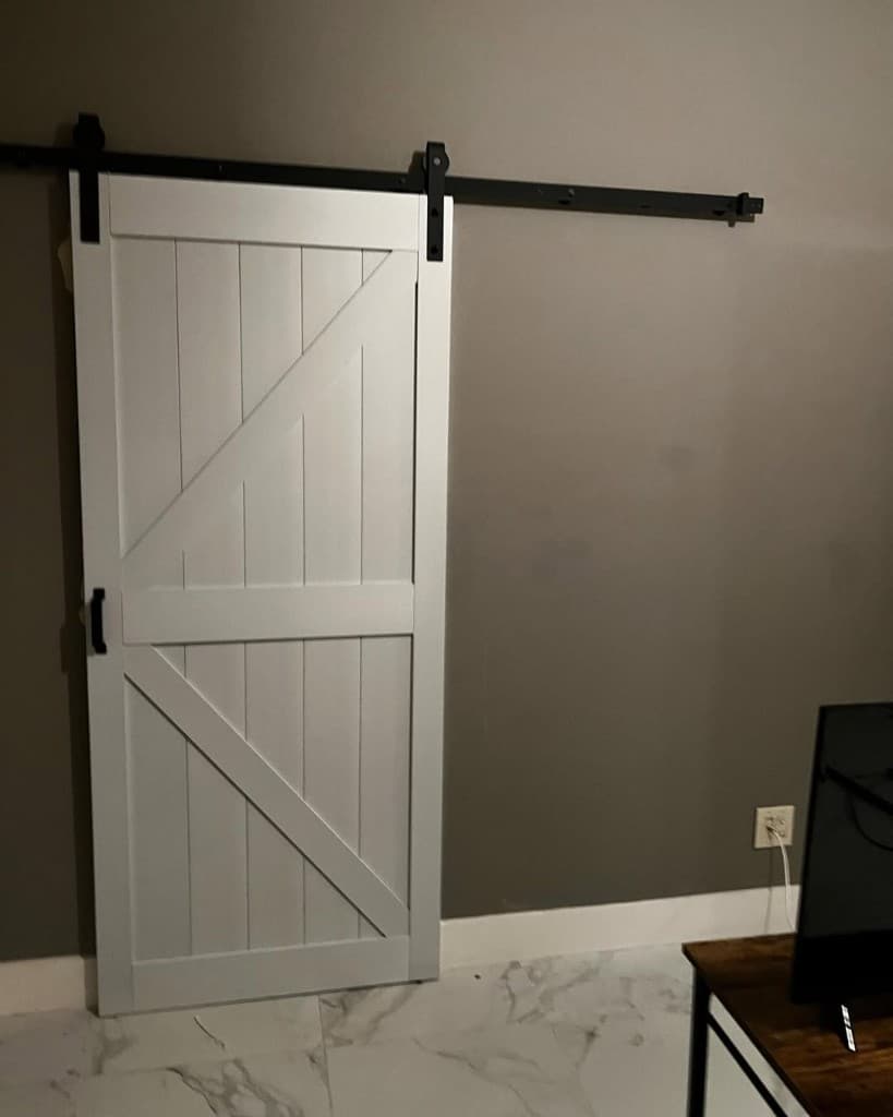 White plank barn door with diagonal brace on black sliding hardware against a charcoal accent wall.