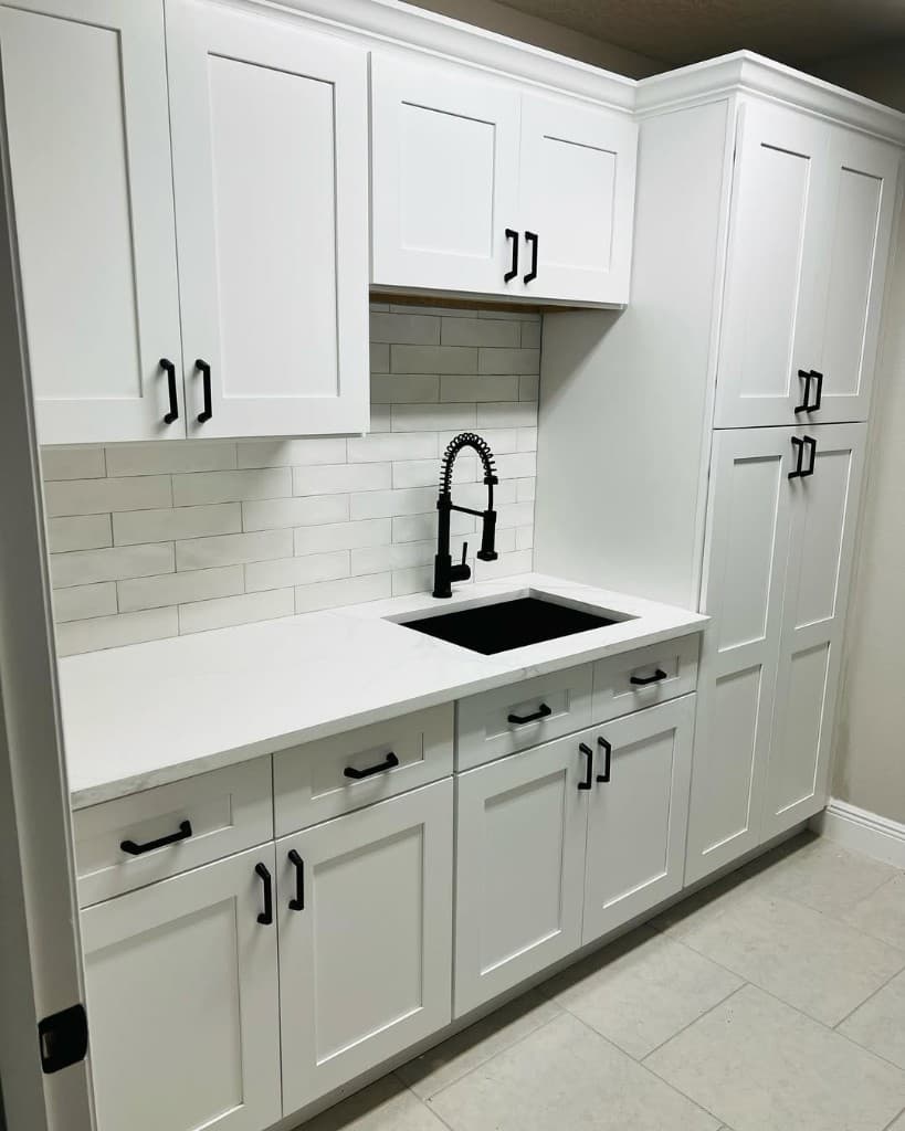 Wide view of remodeled kitchen-laundry space with white cabinets, backsplash, large-format floor tile, and black accents.