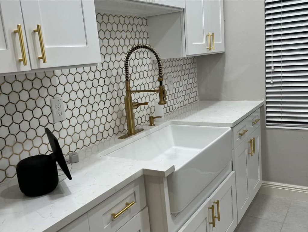 Kitchen corner black smart screen device gold faucet white apron sink honeycomb backsplash white blinds grey wall perspective.