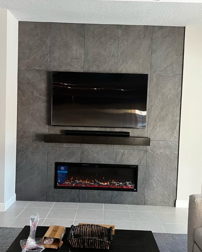 Living wall large grey stone look tile widescreen television wood mantle soundbar electric fireplace beige floor coffee table cardboard.