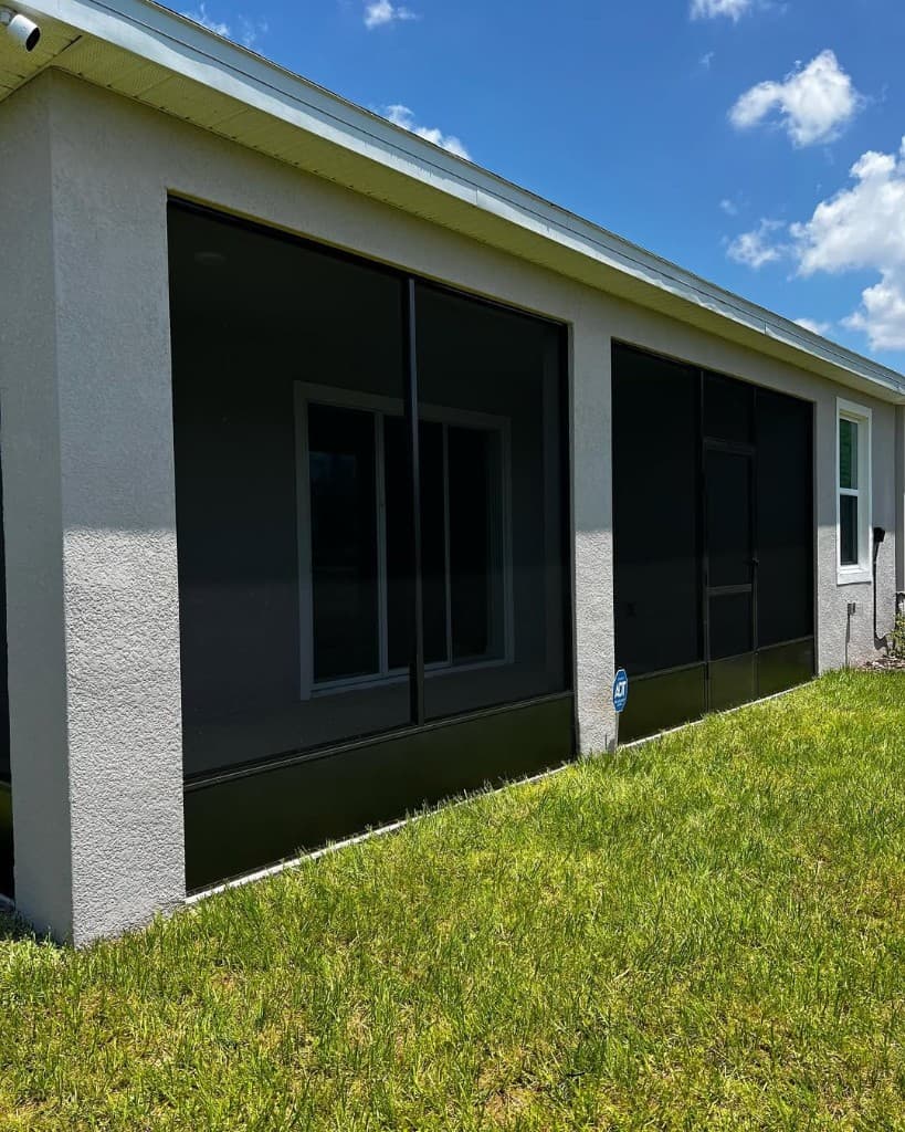 Exterior lanai enclosure with black frame screens, sliding screen door, and grass yard in daylight.