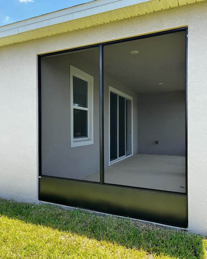 Exterior two panel black screen wall looking into grey patio concrete sliding glass door interior lawn foreground bright.