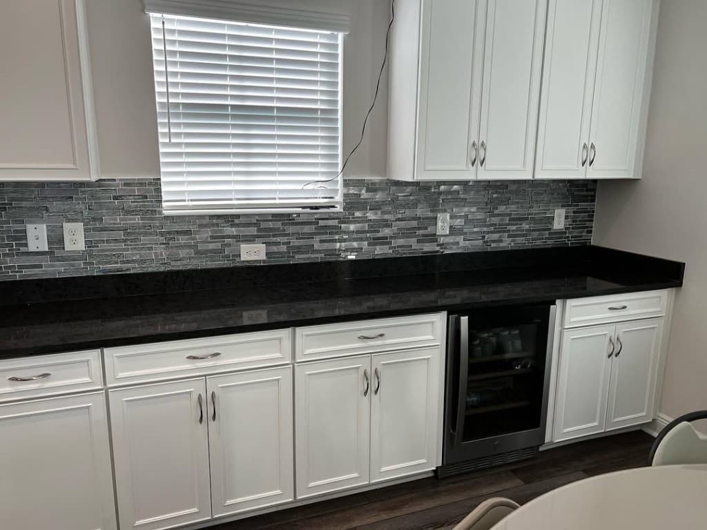 Home bar vignette shaker white cabinets patterned mosaic backsplash black stone counter fridge glass door inserts.